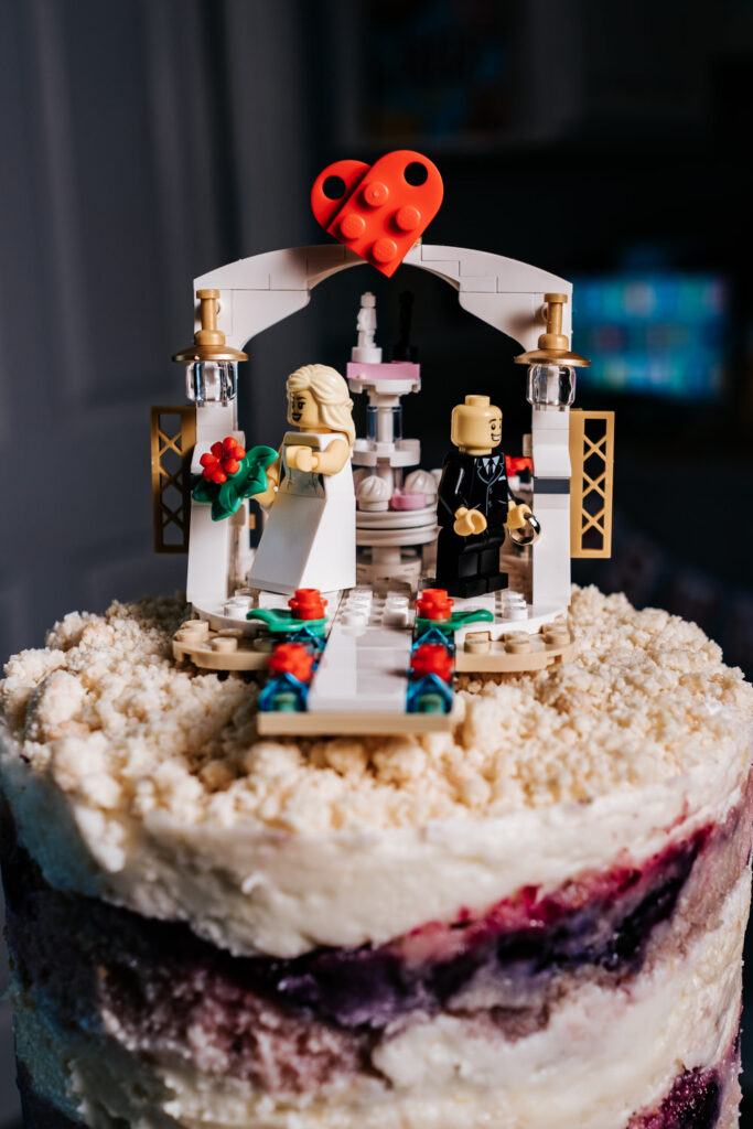 cake topper made of legos with bride and groom under an archway with a heart above it