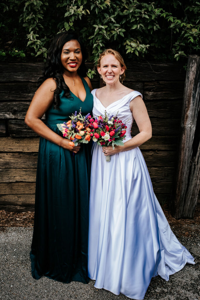 bride in white dress and one bridesmaid in hunter green dress with bouquets smiling at camera