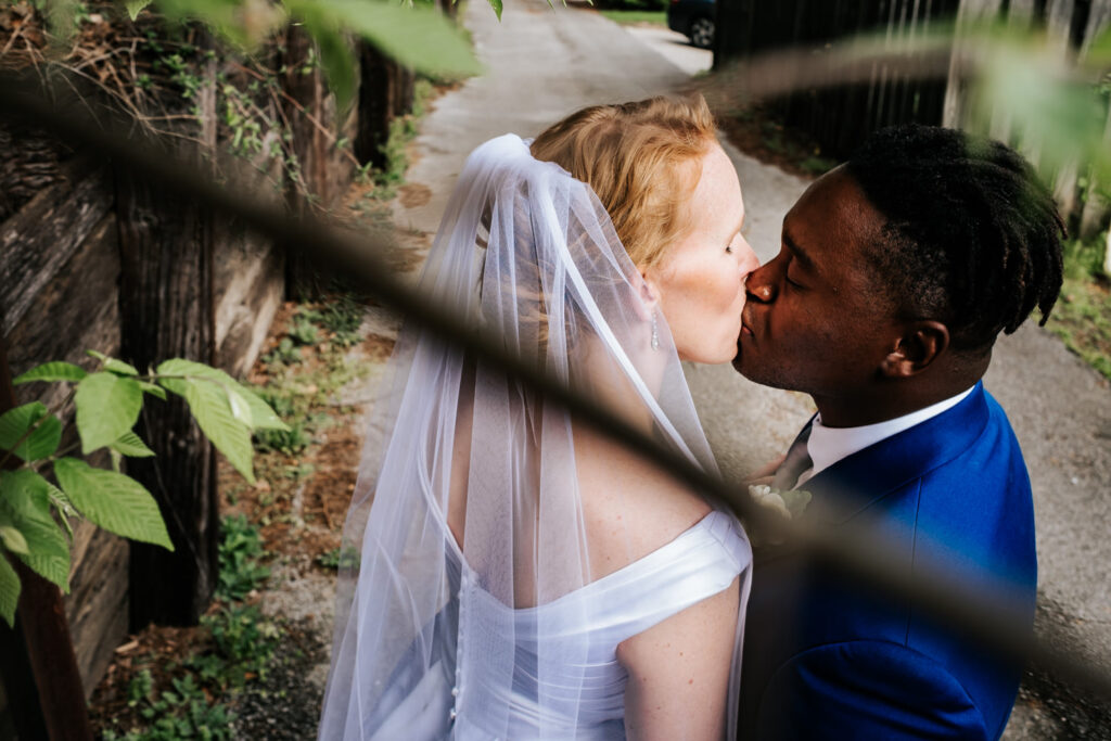 groom and bride kissing through the branches in an alleyway