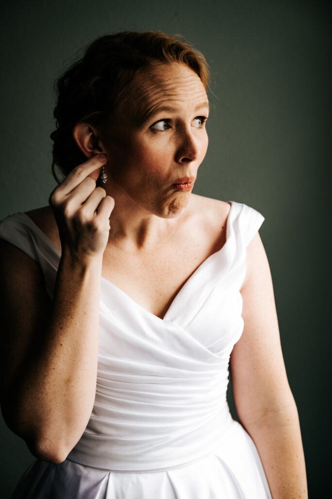 bride in white v-neck dress holding hand at her earlobe making a silly face