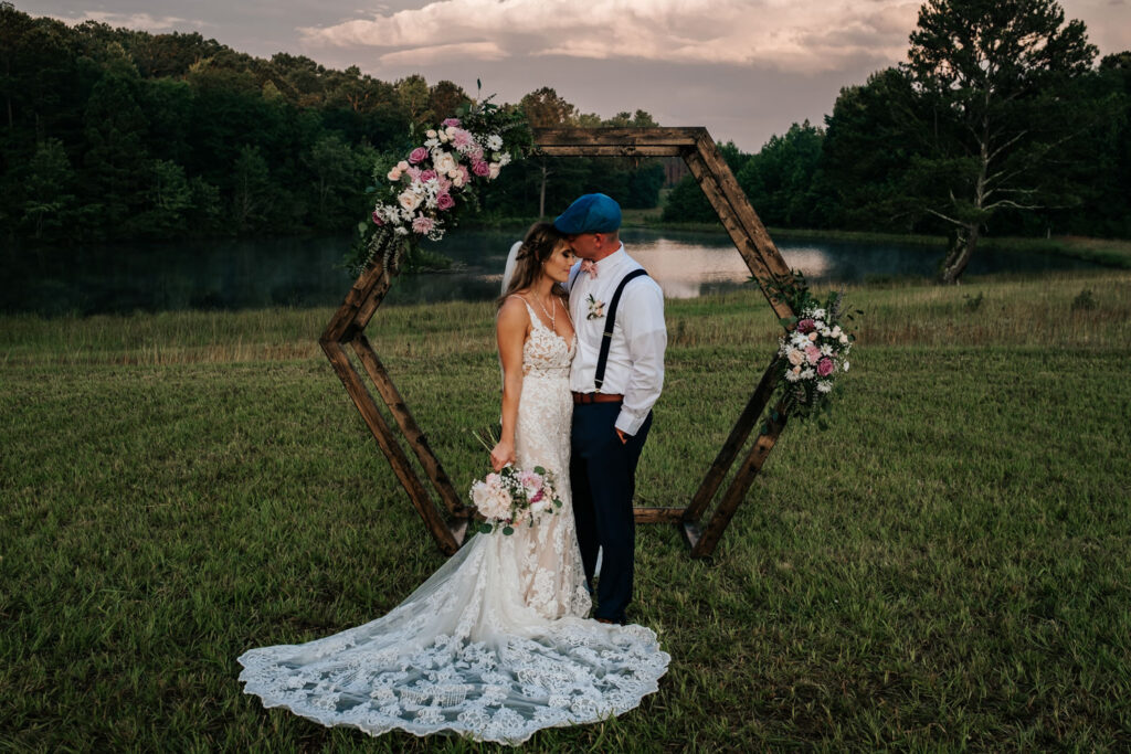 Bride and Groom in front of Hexagon with flowers with groom kissing brides head
