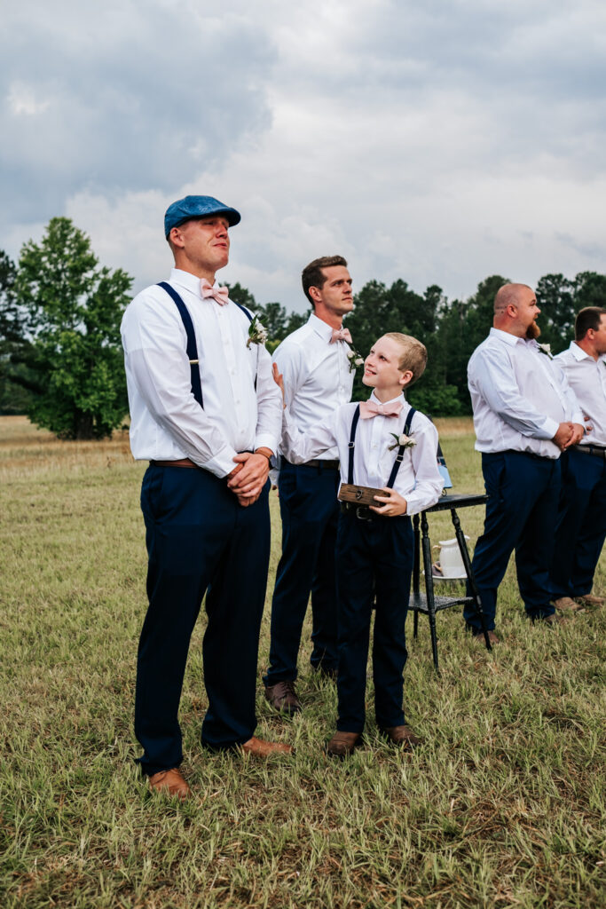 Groom watching and crying while bride walks down the aisle and ring bearer reaching out to comfort him