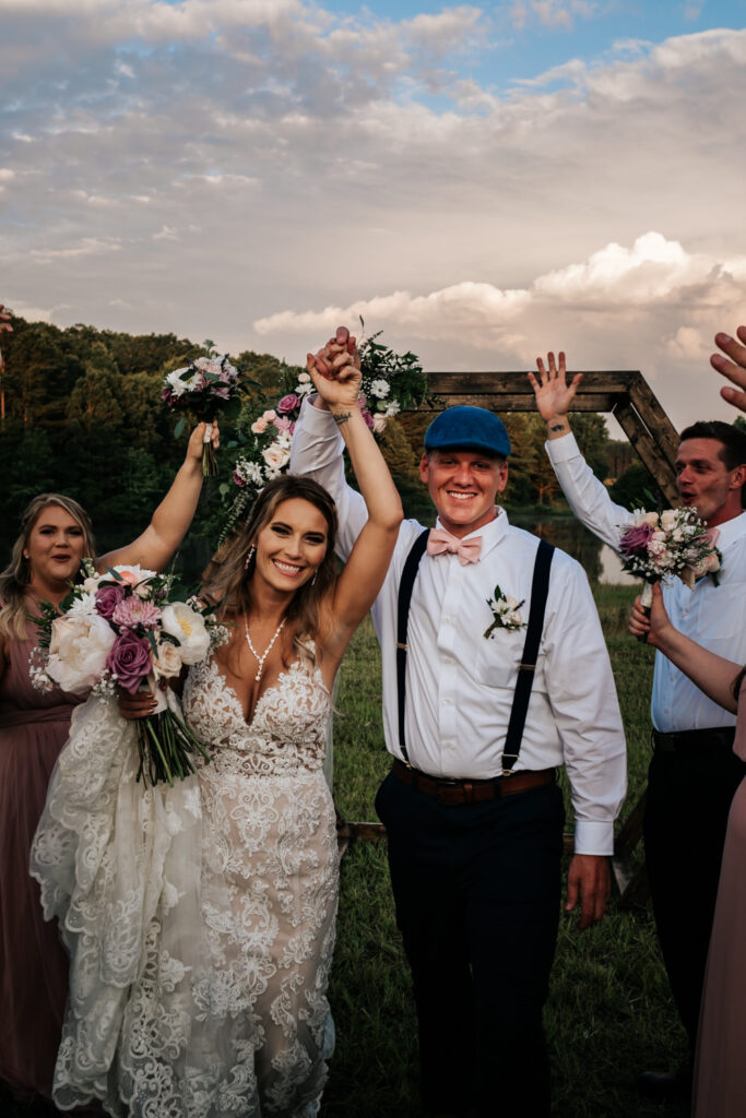 bride and groom walking through bridal party on either side with hands up laughing