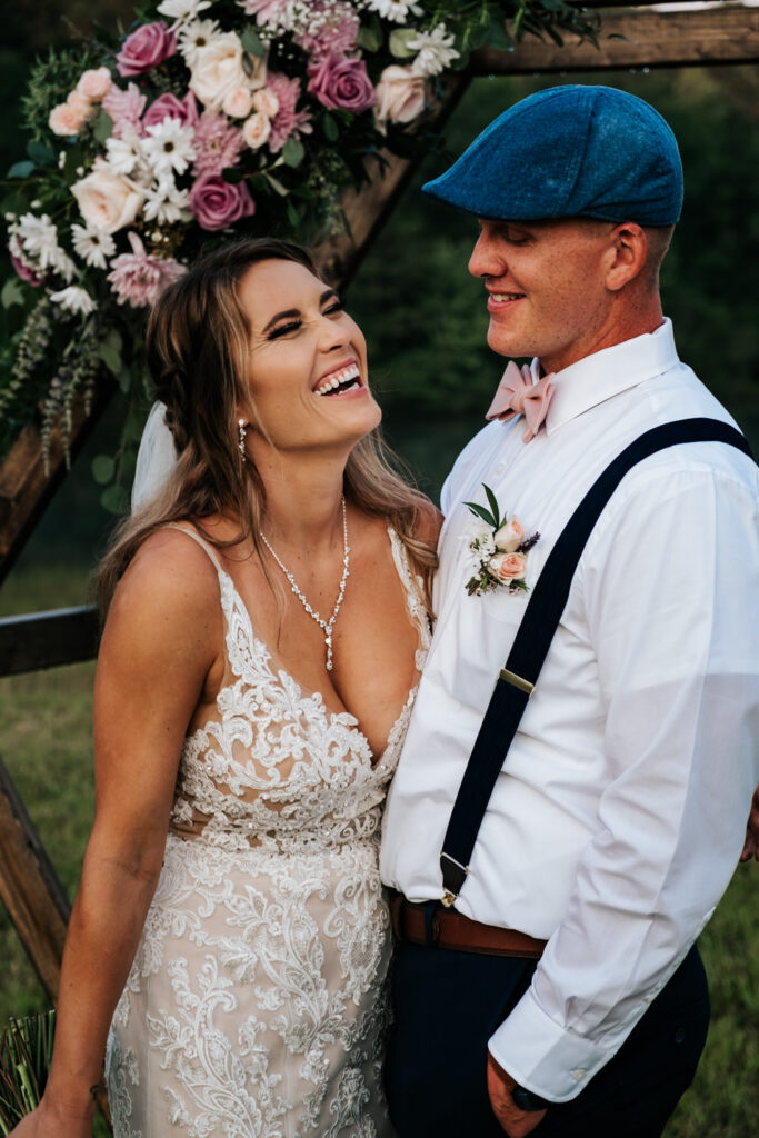 bride in lace dress laughing with groom in blue hat and pink bowtie