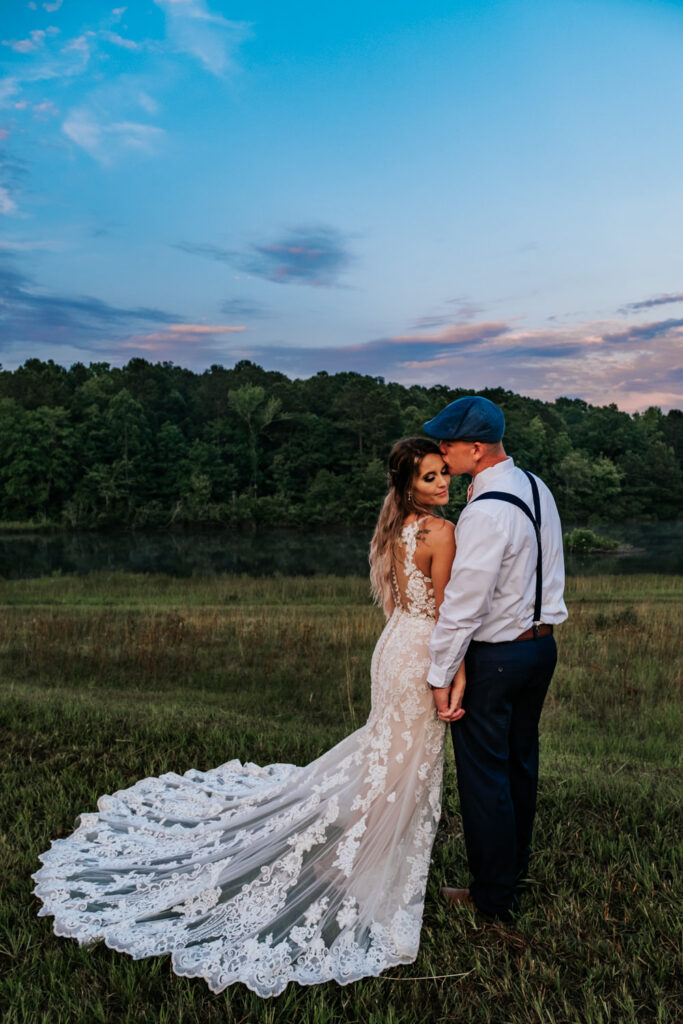 bride in lace dress with long train holding hands with groom in blue hat