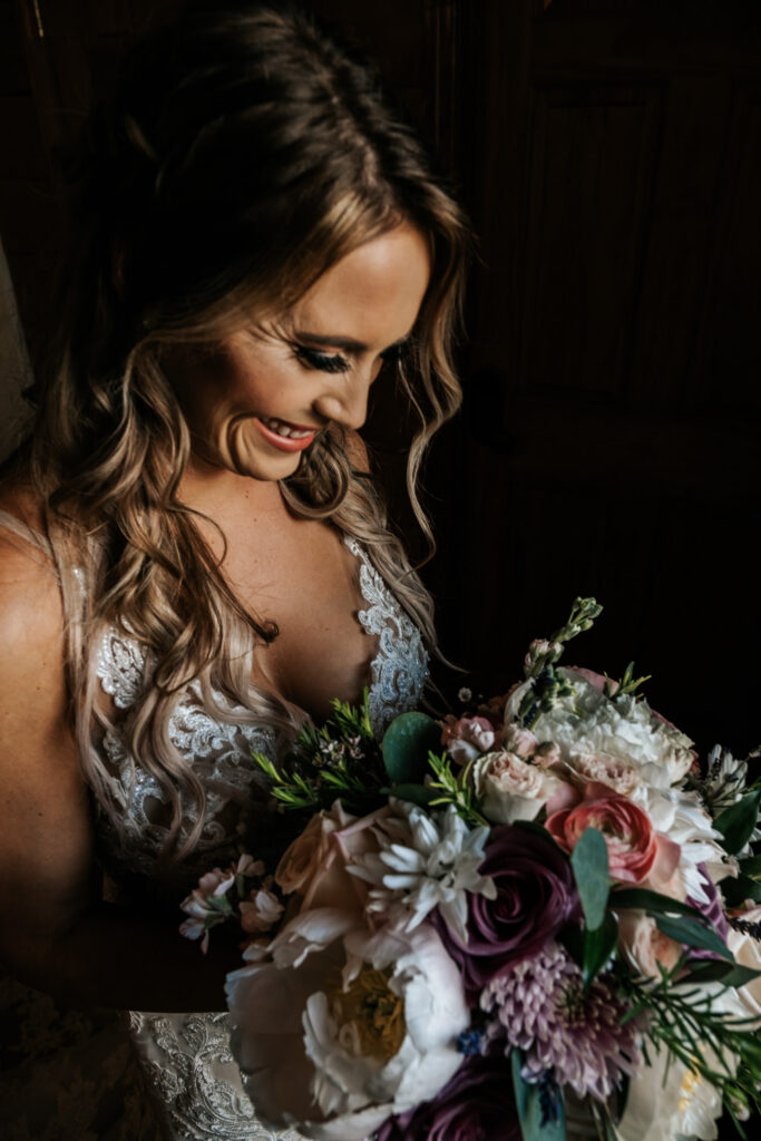 Bride smiling down at bouquet in front of window